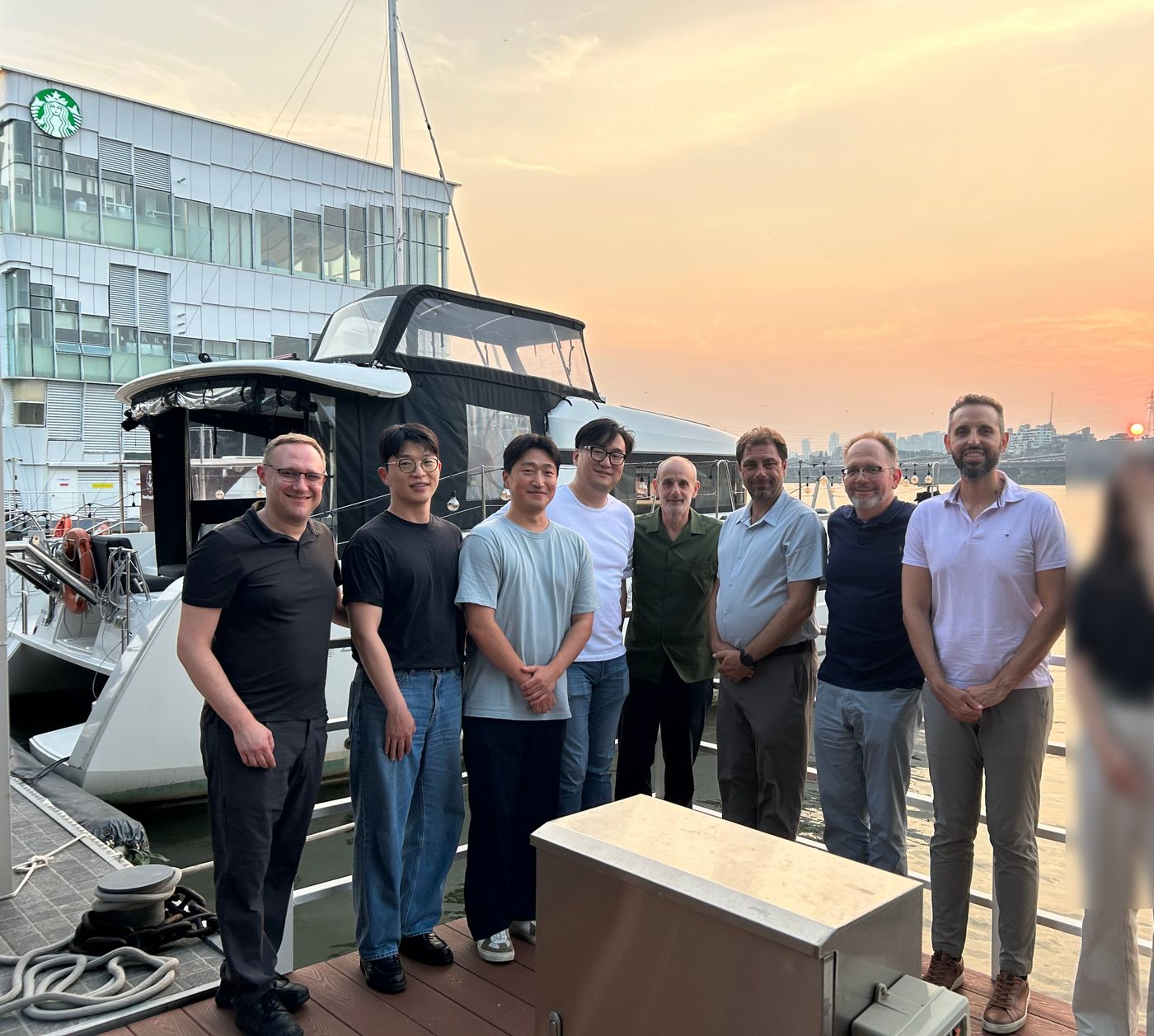 A group posing on a riverside dock at sunset beside a moored boat, with a waterfront building behind them