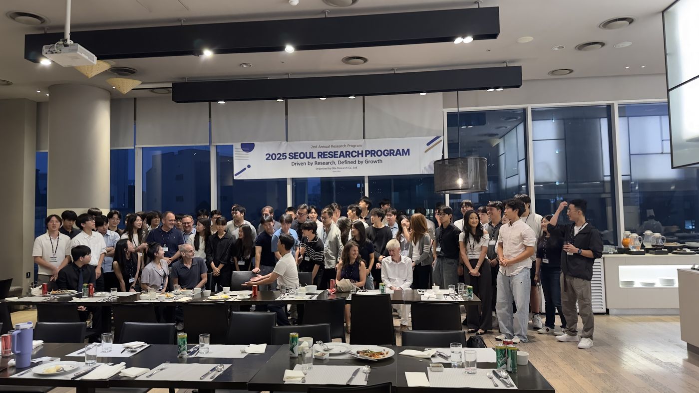 Dozens of students and faculty stand together behind dinner tables beneath a 2025 Seoul Research Program banner