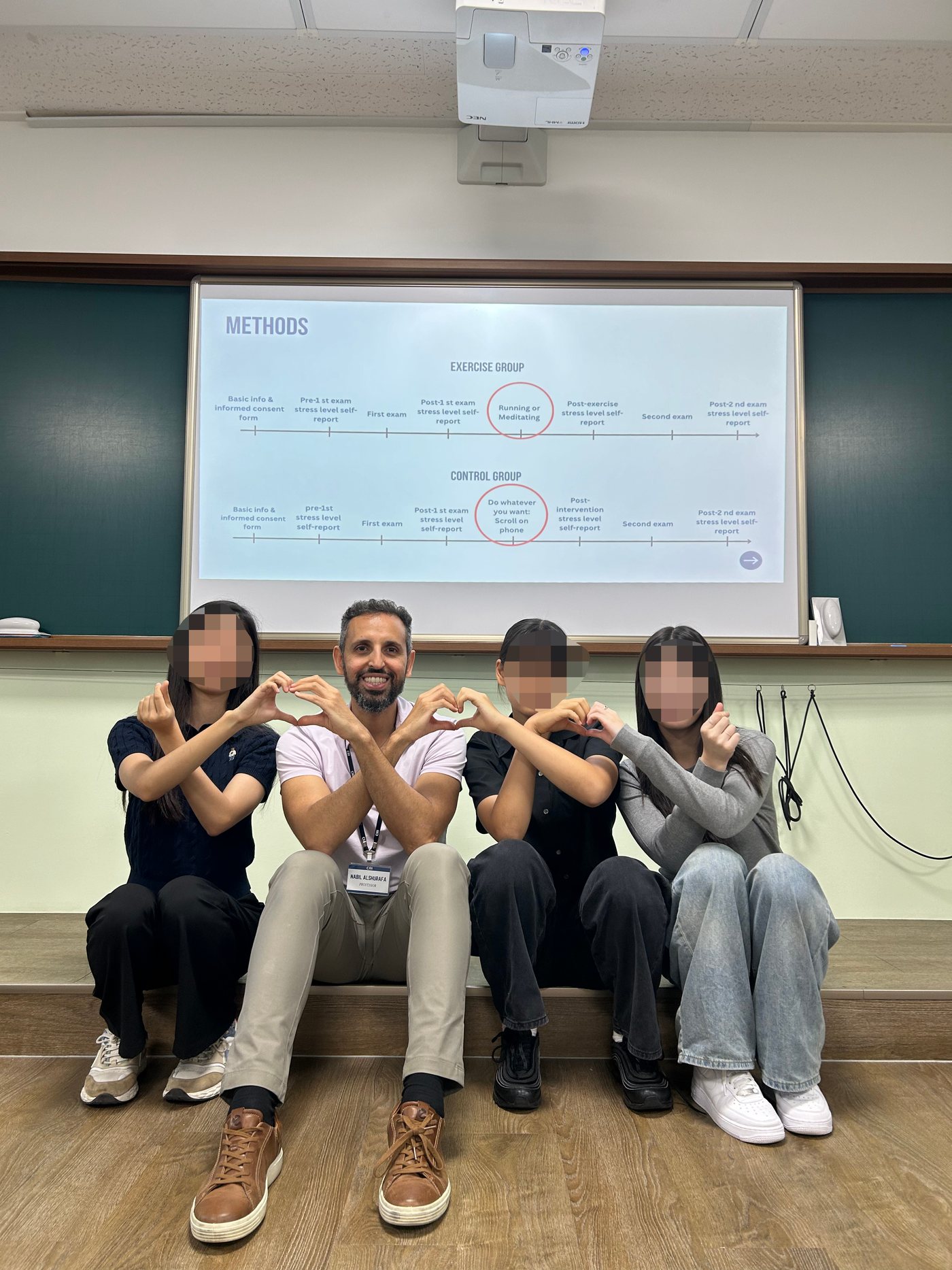 Professor Alshurafa sits with three students, faces blurred, beneath a projected slide showing the study timeline for an exercise group and a control group across two exams