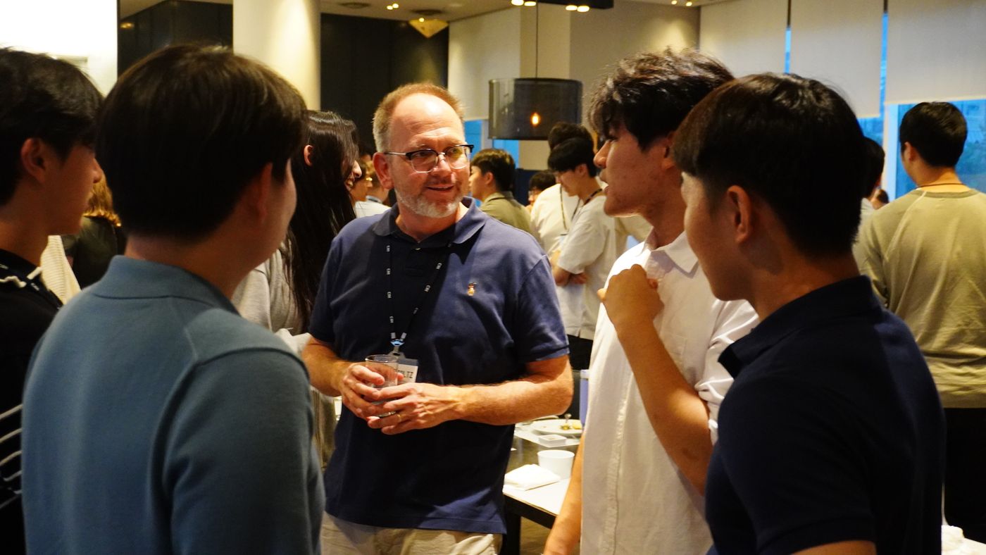 Brian Stoltz, holding a drink, chats with a group of students at an evening gathering