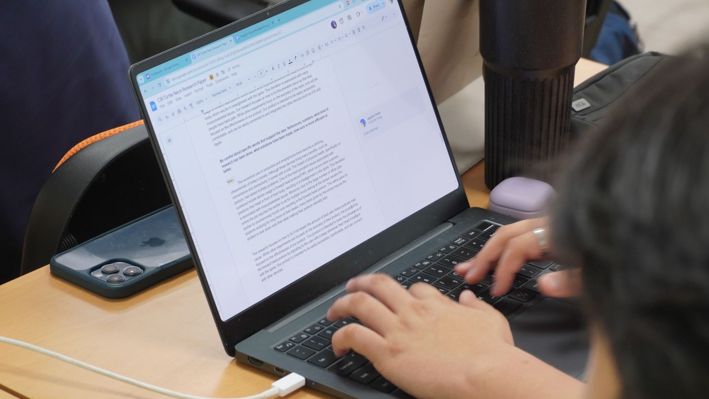 A student types in a Google Docs research paper draft on a laptop