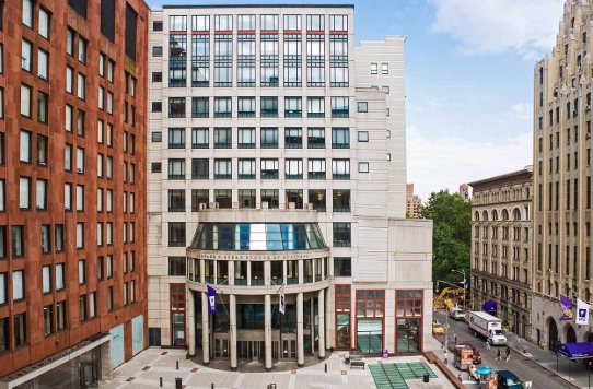Pale stone building with a curved glass rotunda over an entrance inscribed 'Leonard N. Stern School of Business', between brick buildings, with purple NYU flags along the street