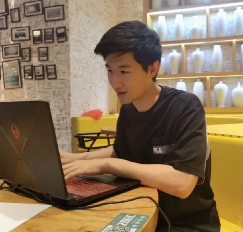 A student in a black T-shirt typing on a laptop at a café table
