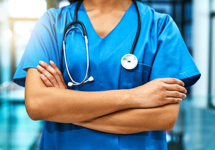 A doctor in blue scrubs with a stethoscope around the neck, arms crossed