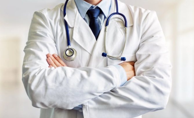 A physician in a white coat with a stethoscope around the neck, arms folded