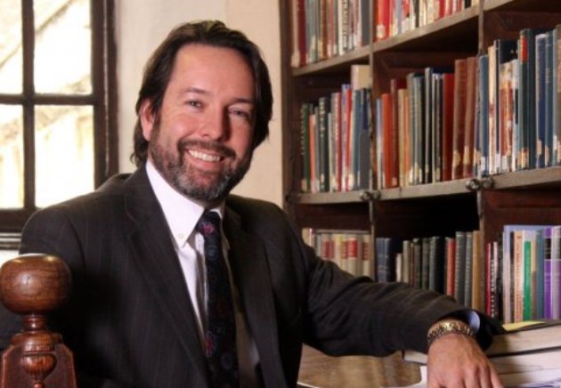 Robin Murphy, smiling, in a dark suit and tie, seated in front of shelves of books