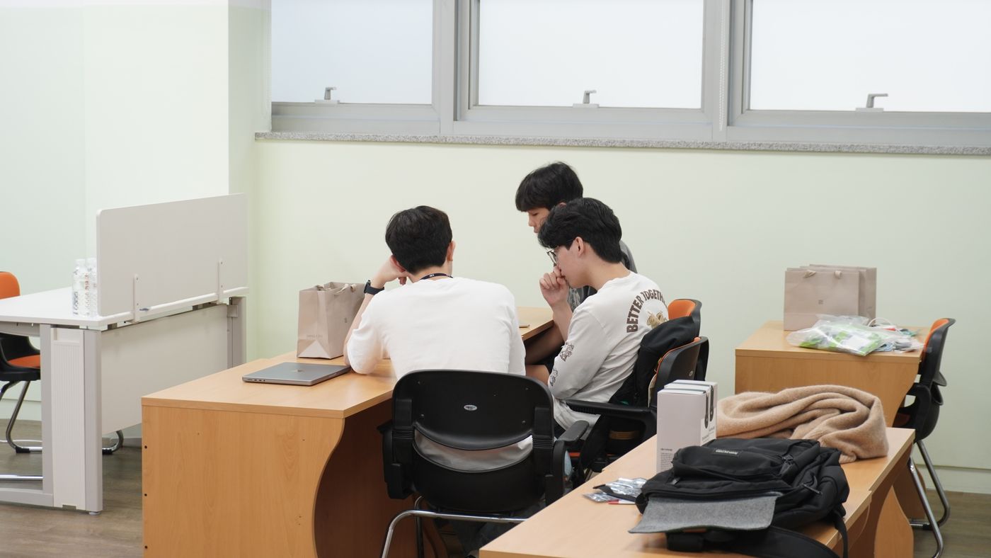 Three students working together at a desk with a laptop in a classroom