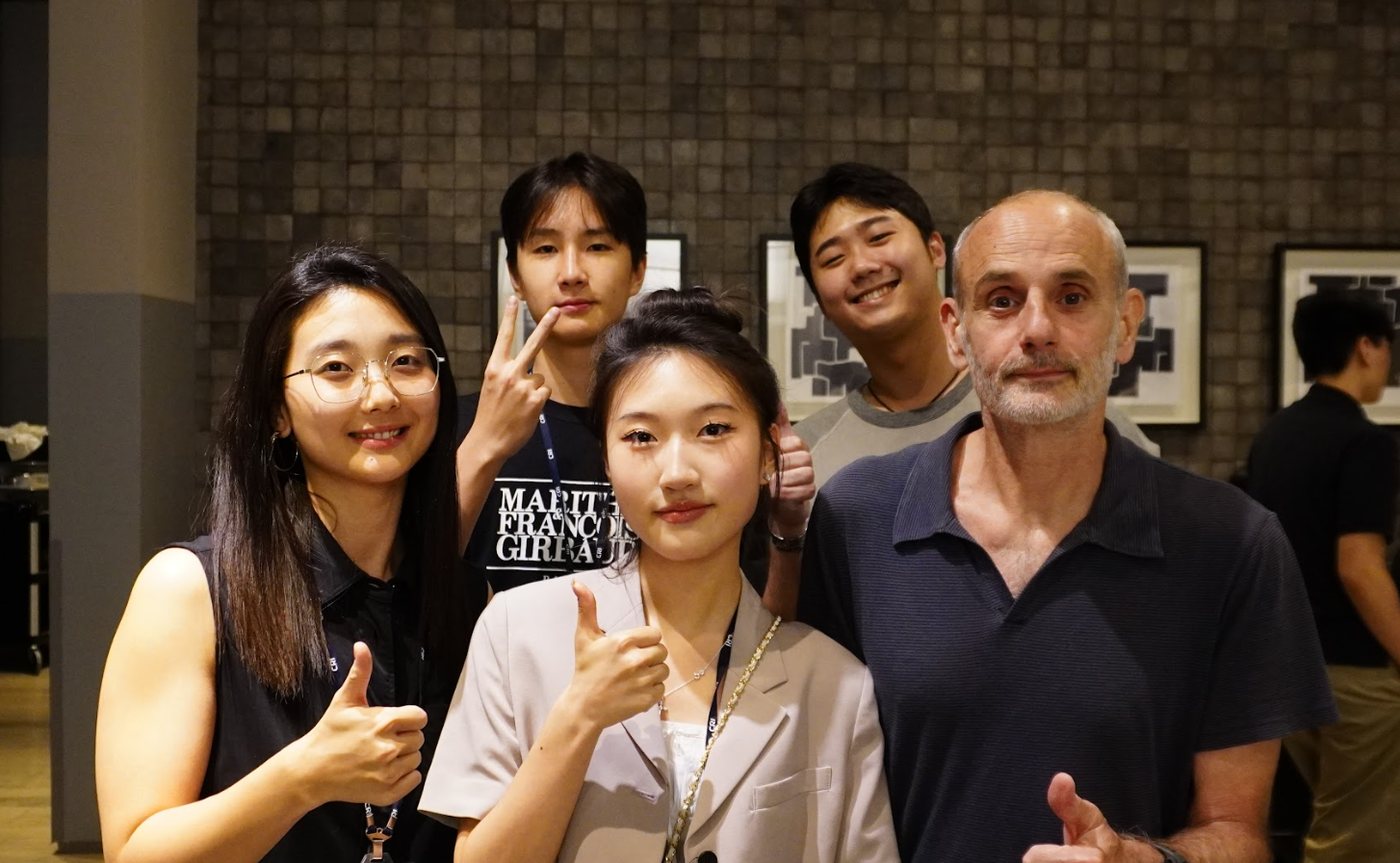 Professor Savoca gives a thumbs-up beside four members of the program in front of a gray tiled wall