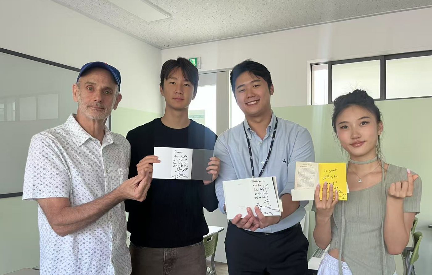Professor Savoca, in a patterned white shirt and blue cap, stands in a classroom with three people who each hold up a handwritten note