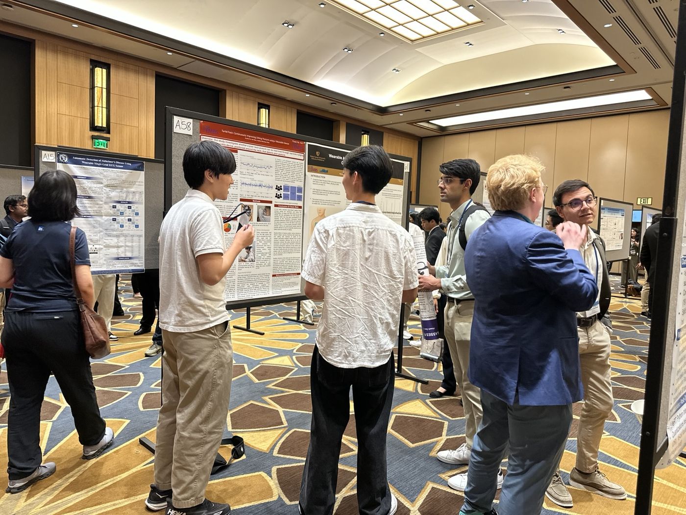 Two students stand at their research poster in a crowded conference hall while attendees look on